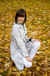 Young woman sits on autumn leaves. Focus on the face.