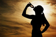 Foto: Beautiful young sporty woman drinking in front of a sunset. Beautiful young sporty woman drinking in front of a sunset.