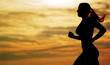 Beautiful young woman running in front of a sunset.