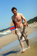 Skimboarder walking along the beach. Skimboarder walking along the beach.