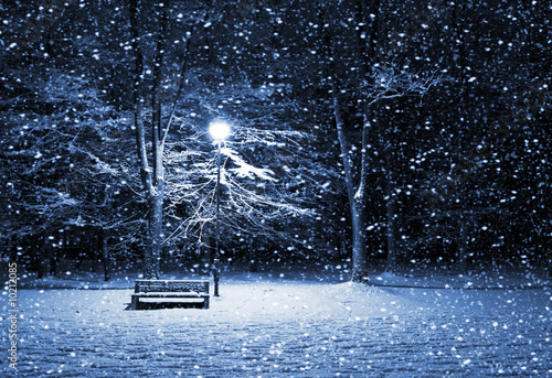View of bench and shining lantern through snowing. Night shot..