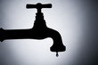 a silhouette of a leaking tap against bluish background