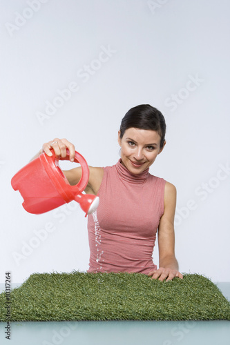 Photo: Beautiful girl watering artificial grass Beautiful girl watering artificial grass