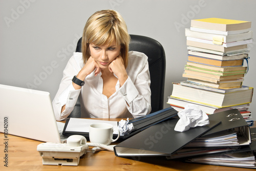 Photo: Dissatisfied business lady or student sitting at a busy desk. Dissatisfied business lady or student sitting at a busy desk.