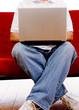 A man sitting on a red couch working on a laptop computer