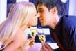 Young happy couple with champagne kissing at restaurant