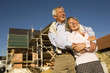 Senior couple embracing in front of construction site, laughing, low angle view