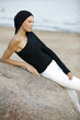 Young woman leaning on rock at beach, looking away, side view