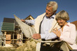 Senior couple holding plan in front of partially built house