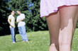 Two young men standing in garden, focus on woman's legs at foreground