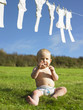 Baby sitting and holding clothes peg.