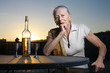 Elderly woman with bottle of white wine outdoors at sunset.
