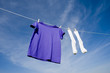 A purple t-shirt on a clothesline with a pair of white socks