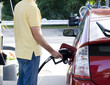 Photo: Man standing at petrol tank and is filling up his red car Man standing at petrol tank and is filling up his red car
