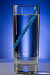 Glass with pure water with blue straw on a blue background