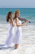two young woman play violins on beach in the water