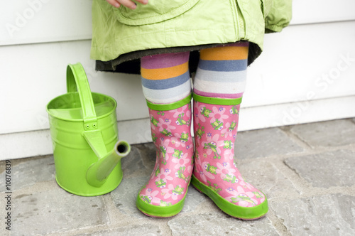 Photo: Little girl in boots, close-up, green watering can Little girl in boots, close-up, green watering can