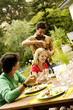 2 young men and a woman sitting at garden table, man opening wine bottle