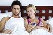 Young couple in bed, watching TV
