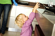 Little girl in kitchen trying to catch a frying pan on stove, indoors