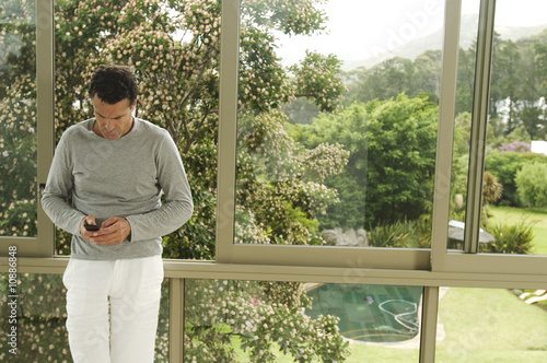Photo: Man leaning against bay window, using mobile phone Man leaning against bay window, using mobile phone