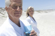 Couple in bathrobe on the beach, man with glass of water in foreground