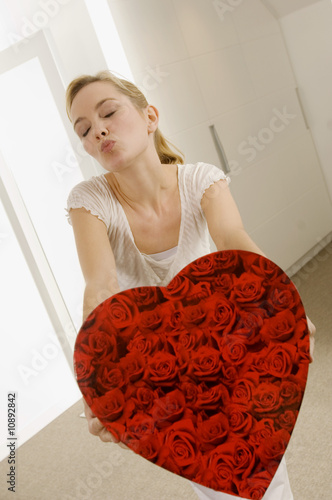 Photo: Young woman holding a heart shape gift and puckering her lips Young woman holding a heart shape gift and puckering her lips