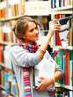 Foto: Female university student selecting book from shelf in a library Female university student selecting book from shelf in a library