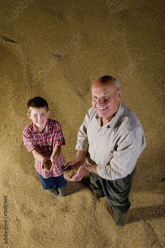 Photo: Farmer and grandson holding grains on grain heap Farmer and grandson holding grains on grain heap