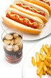 a glass of cola with ice, french fries and three classic hotdogs