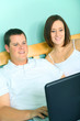 Busy Couple Using Laptop On Bed