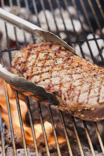 Photo: beef steak on a barbecue with barbecue tongs beef steak on a barbecue with barbecue tongs