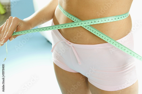 Photo: hand holding tape measure around waist (detail) hand holding tape measure around waist (detail)