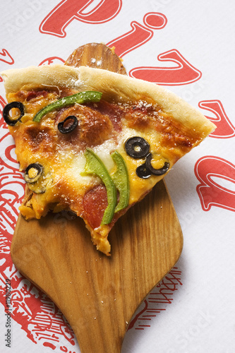 Photo: piece of pizza with cheese, salami, peppers, olives on server piece of pizza with cheese, salami, peppers, olives on server