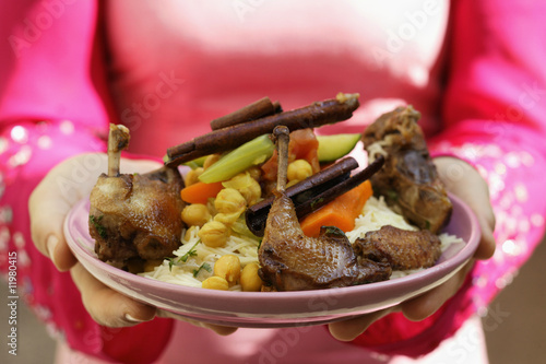 Photo: woman serving roast pigeon with vegetables on noodles (morocco) woman serving roast pigeon with vegetables on noodles (morocco)