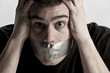 Man with mouth covered by masking tape preventing speech..