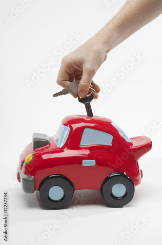 Photo: Hand Putting Car Keys in Car Shaped Piggy Bank Hand Putting Car Keys in Car Shaped Piggy Bank