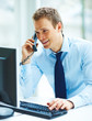 Young busineass man speaking on the phone while working on a com