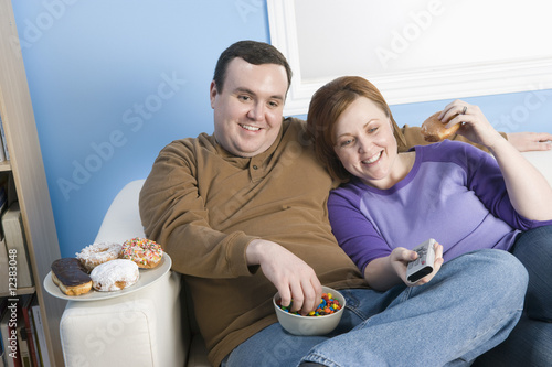 Photo: Overweight couple watching television on sofa Overweight couple watching television on sofa