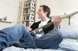 Photo: Man playing guitar on the bed. Man playing guitar on the bed.