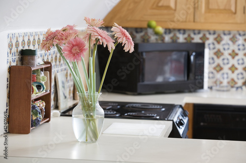 Photo: A flower vase with pink daisies in a kitchen. A flower vase with pink daisies in a kitchen.
