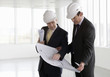 Two architects wearing hard hats looking at plans