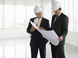 Two architects wearing hard hats looking at plans