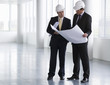 Two architects wearing hard hats looking at plans