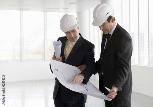 Photo: Two architects wearing hard hats looking at plans Two architects wearing hard hats looking at plans