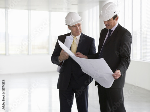 Photo: Two architects wearing hard hats looking at plans Two architects wearing hard hats looking at plans
