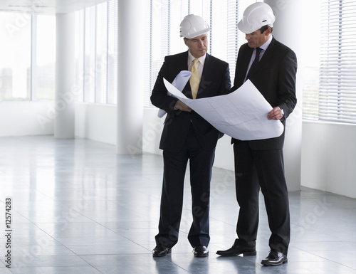 Photo: Two architects wearing hard hats looking at plans Two architects wearing hard hats looking at plans