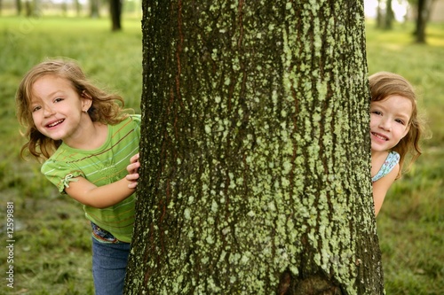 Photo: Two twin little girls playing in tree trunk Two twin little girls playing in tree trunk