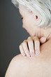 A senior woman applying moisturising cream to her shoulder