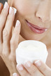 A middle-aged woman holding a pot of moisturising cream